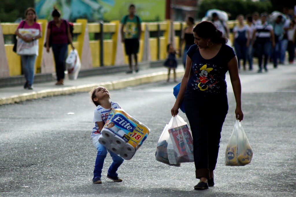 A Venezuelan child carries a pack of toilet paper next to a woman as they cross the Colombian-Venezuelan border over the Simon Bolivar international bridge, after shopping and taking advantage of the temporary border opening in San Antonio del Tachira, Venezuela, July 10, 2016 REUTERS/Carlos Eduardo Ramirez - RTSHA1T