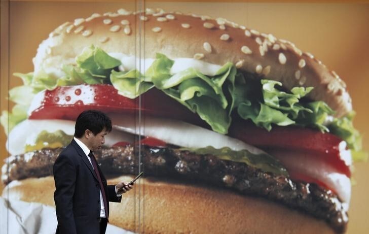 A man holding his mobile phone walks past an advertisement board for a hamburger outside a fast food shop in Tokyo, March 31, 2014. Japanese business confidence improved in the three months to March for a fifth straight quarter, a central bank survey showed, but the pace of recovery slowed and sentiment is seen weakening in the following quarter due to worries that a sales tax hike will dent growth. Picture taken March 31, 2014. REUTERS/Yuya Shino (JAPAN - Tags: BUSINESS POLITICS FOOD)