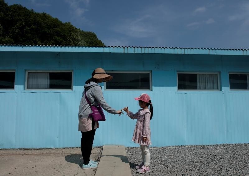 A girl and woman gesture to make a promise over a cement block symbolising a border line as they mimic a handshake between North Korean leader Kim Jong Un and South Korean President Moon Jae-in at the summit in late April, at the replica of the truce village of Panmunjom at a movie studio in Namyangju, South Korea May 8, 2018. Picture taken on May 8, 2018.