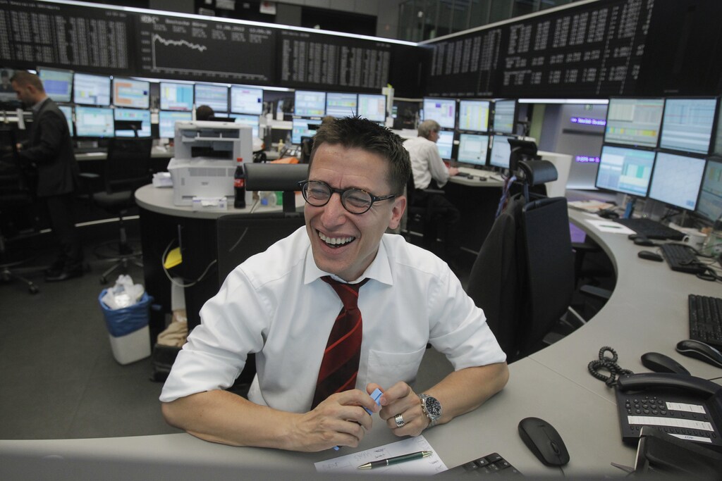 A trader smiles as he works at his desk in front of the DAX board at the Frankfurt stock exchange June 11, 2012. REUTERS/Alex Domanski (GERMANY - Tags: BUSINESS) - RTR33FBZ
