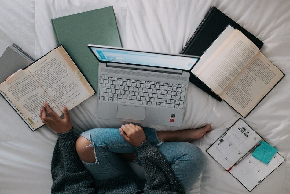 Image of person studying on a bed with laptop and books