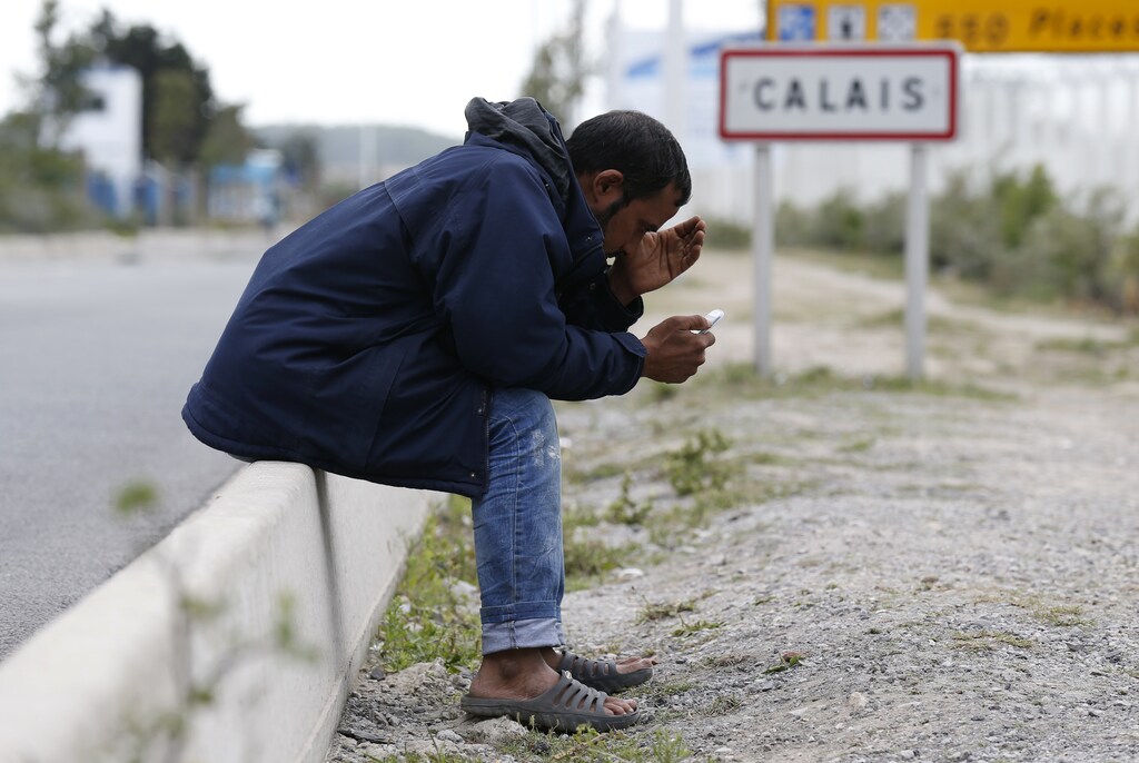 A migrant looks at his mobile phone as he sits near a road sign on the main access route to the Ferry harbour Terminal in Calais, northern France, July 30, 2015. Migrants massed around the entrance to the Channel Tunnel said on Thursday they would keep trying to sneak across to Britain, undaunted by the arrival of 120 extra riot police on the French side. A police officer said the number of migrants trying to enter Britain eased slightly overnight compared to earlier in the week, with about 800 migrants around the site and some 300 intercepted by police. REUTERS/Pascal Rossignol - RTX1MFVL