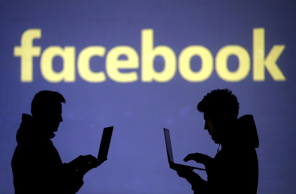 Silhouettes of laptop users are seen next to a screen projection of Facebook logo in this picture illustration taken March 28, 2018. REUTERS/Dado Ruvic/Illustration - RC1EC52FC080