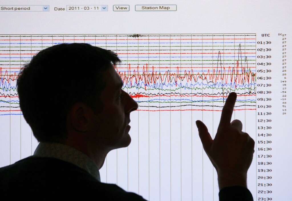 A seismologist poses for the media as he points to a seismographic graph showing the magnitude of the earthquake in Japan, on a monitor at the British Geological Survey office in Edinburgh, Scotland March 11, 2011. The biggest earthquake on record to hit Japan struck the northeast coast on Friday, triggering a 10-metre tsunami that swept away everything in its path, including houses, ships, cars and farm buildings.