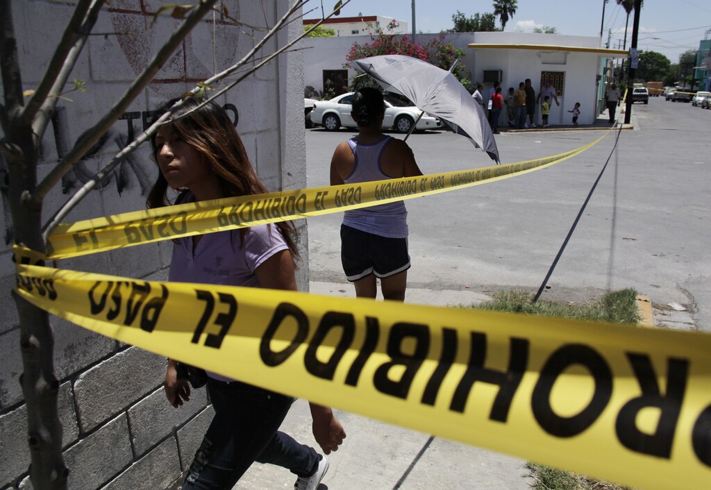Pedestrians walk around yellow police tape at a crime scene in Monterrey.