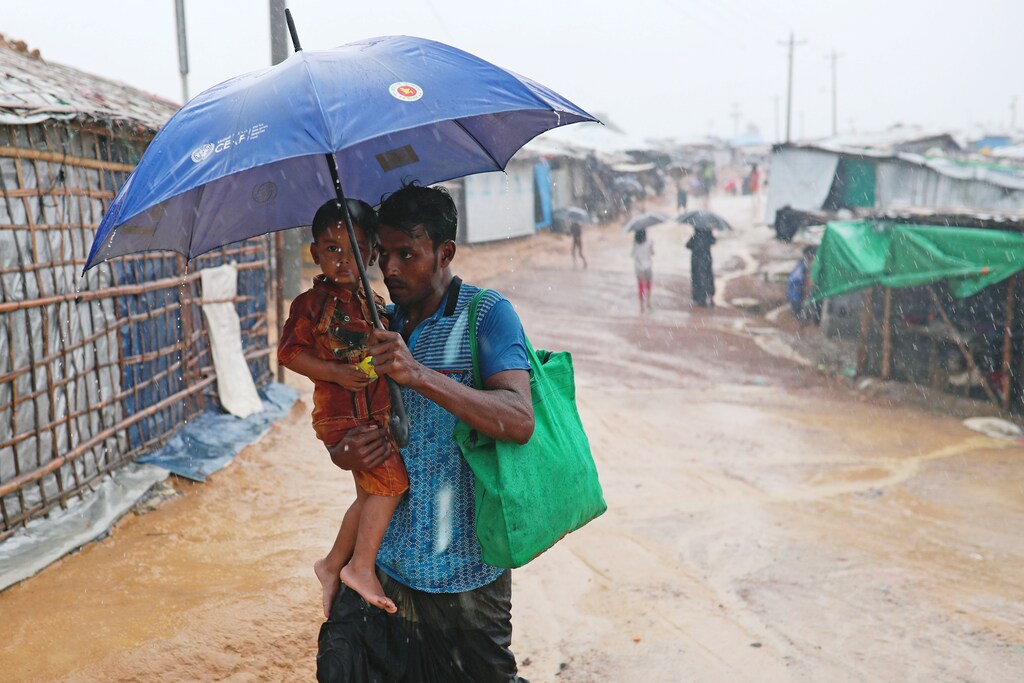Rohingya refugee man with child returns to his shelter in Kutupalong camp during heavy rain in Cox's Bazar, Bangladesh, July 4, 2018. REUTERS/Mohammad Ponir Hossain - RC1BF34787B0