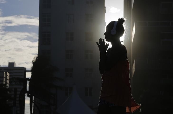 A woman listens to music as the sun sets as seen between buildings on Boa Viagem beach in Recife June 30, 2014. In a project called "On the Sidelines" Reuters photographers share pictures showing their own quirky and creative view of the 2014 World Cup in Brazil. REUTERS/Brian Snyder (BRAZIL - Tags: SPORT SOCCER WORLD CUP SOCIETY ENVIRONMENT)