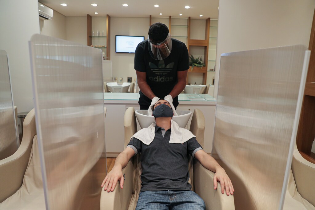 A hairdresser wearing protective mask and face shield dries customer's hair between acrylic walls set up for social distancing at a hair salon, as the city eases the restrictions imposed to control the spread of the coronavirus disease (COVID-19), in Sao Paulo, Brazil July 6, 2020. REUTERS/Amanda Perobelli - RC2WNH9S3GB0
