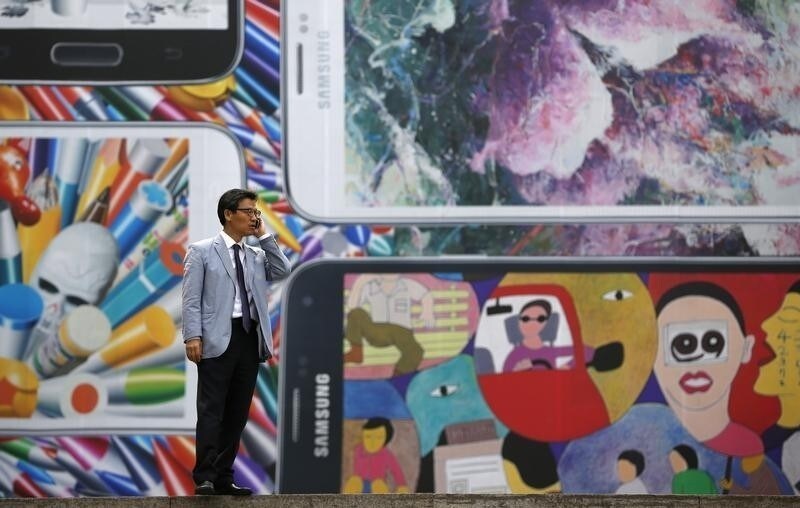 A man uses his mobile phone in front of a giant advertisement promoting Samsung Electronics' new Galaxy S5 smartphone, at an art hall in central Seoul April 15, 2014. Samsung Electronics Co Ltd's new Galaxy S5 smartphone should outsell its predecessor and defy predictions that the South Korean titan's latest model will struggle in a tough market for high-end handsets, Yoon Han-kil, senior vice president of Samsung's product strategy team, told Reuters in an interview. Picture taken on April 15, 2014. To match Interview SAMSUNG-ELEC-SALES/ REUTERS/Kim Hong-Ji (SOUTH KOREA - Tags: BUSINESS SCIENCE TECHNOLOGY TELECOMS) - RTR3LG96
