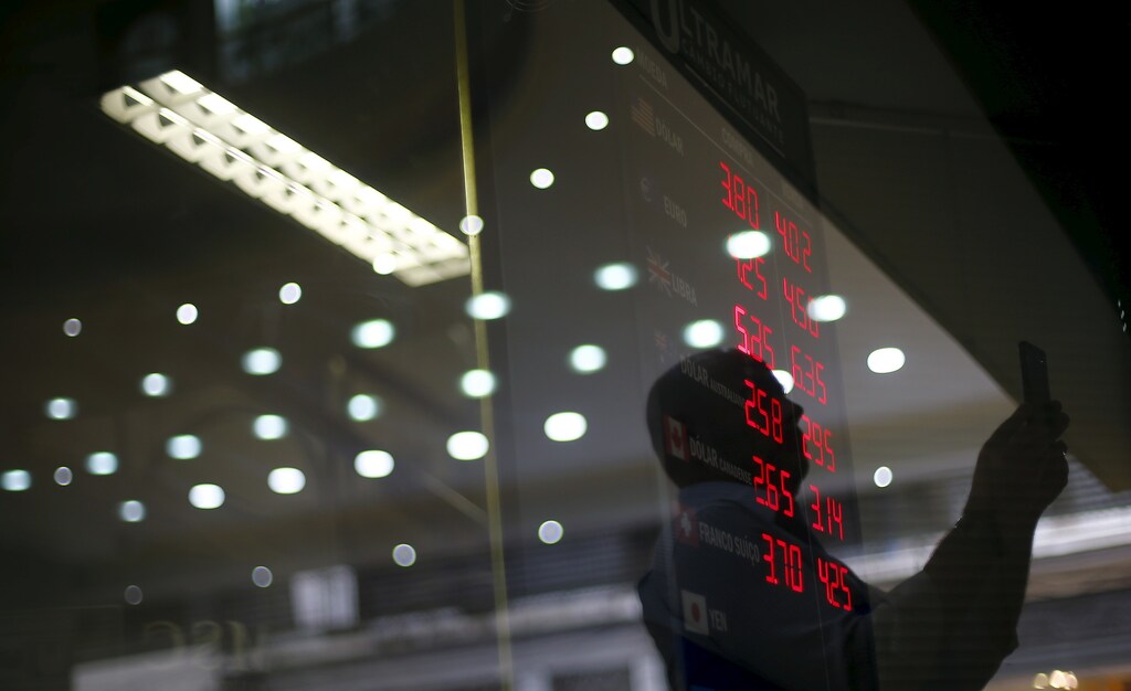 A man is reflected on the glass as he takes pictures of a board showing the Real-U.S. dollar and several foreign currencies exchange rates in Rio de Janeiro, Brazil, September 10, 2015. One thing is clear for Brazil's economy after its credit rating was downgraded to junk: political leaders now have little choice but to push ahead with painful austerity measures if they hope to regain market confidence. Standard & Poor's on Wednesday stripped Brazil of its hard-won investment grade rating, moving sooner than the government and investors had expected. Although investors expected a downgrade at some point, they still sold off Brazilian assets early on Thursday. Stocks suffered modest losses while the currency, the real, fell nearly 3 percent to a 13-year low of 3.9 per dollar. REUTERS/Ricardo Moraes - RTSJ0I