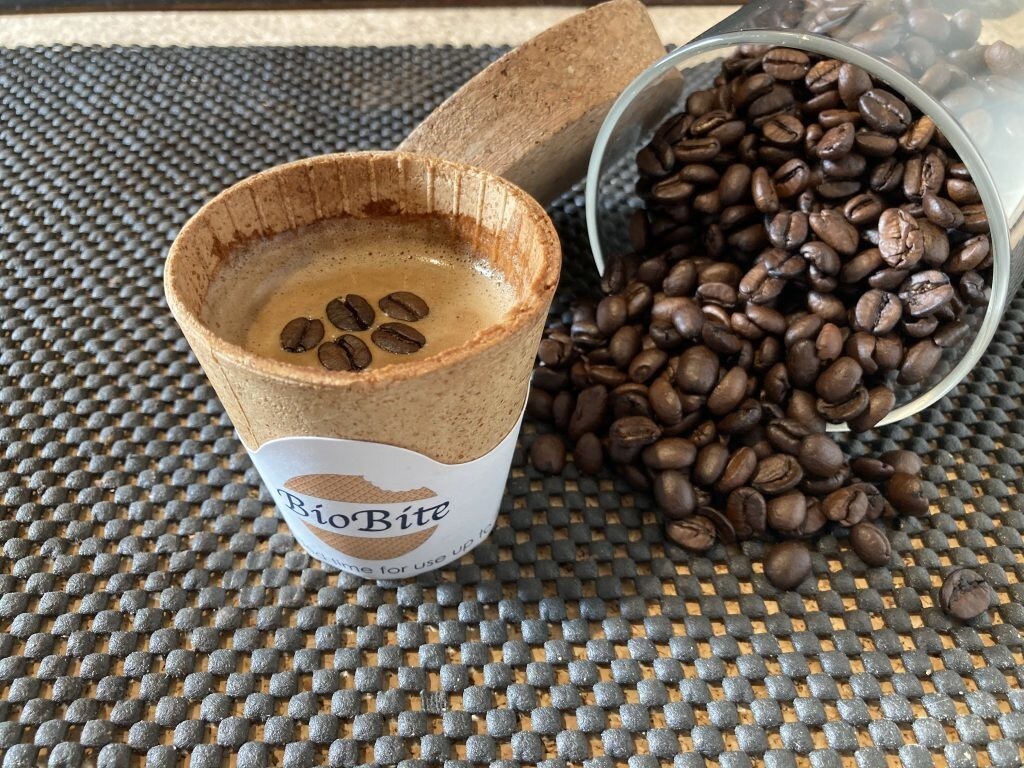 An edible coffee cup with some coffee in next to a small pile of coffee beans