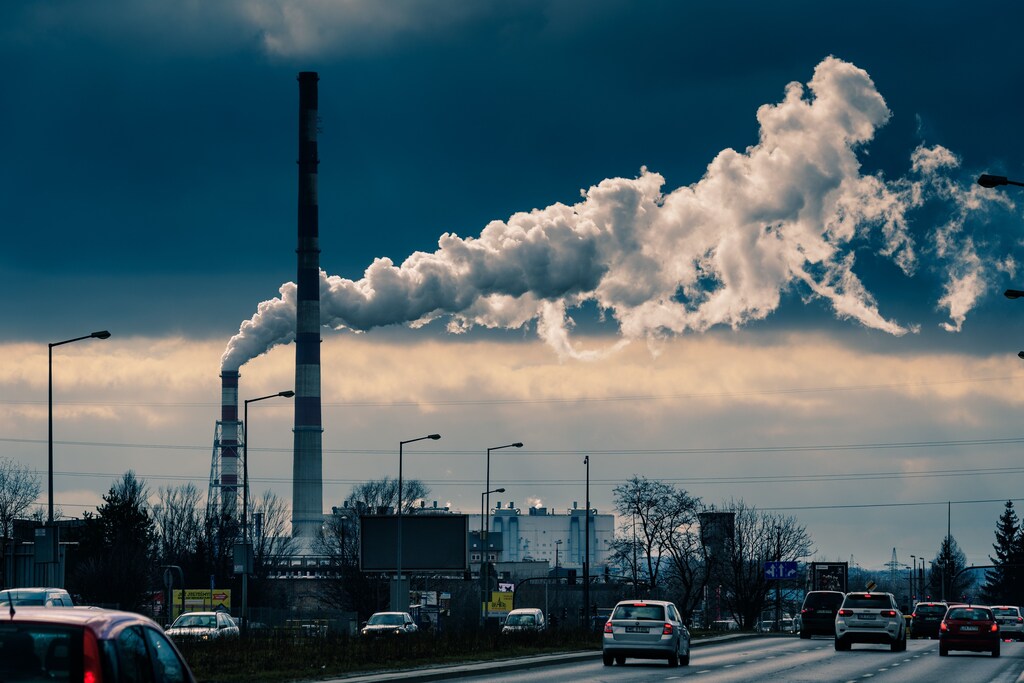 Smoke emerging from a factory chimney with cars driving on a road in front - pollution