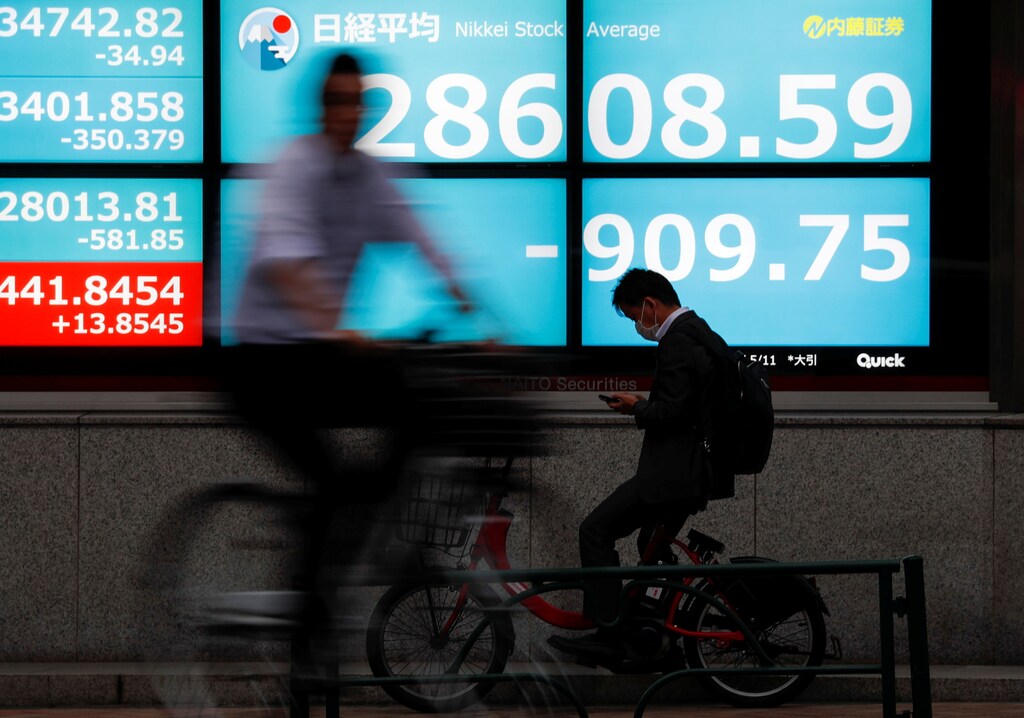 People ride bicycles past a screen displaying Nikkei share prices