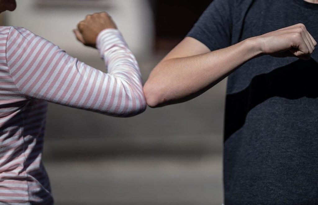 Two people meeting with an elbow tap, a common way to greet amidst the COVID-19 pandemic.