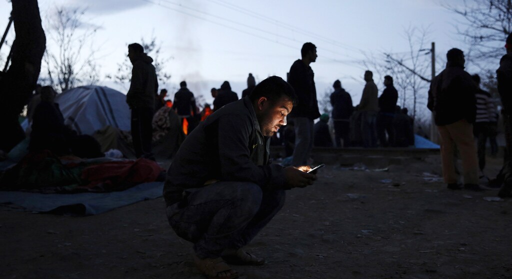 A migrant checks his smart phone as he waits at the Greek-Macedonian border in 2015.