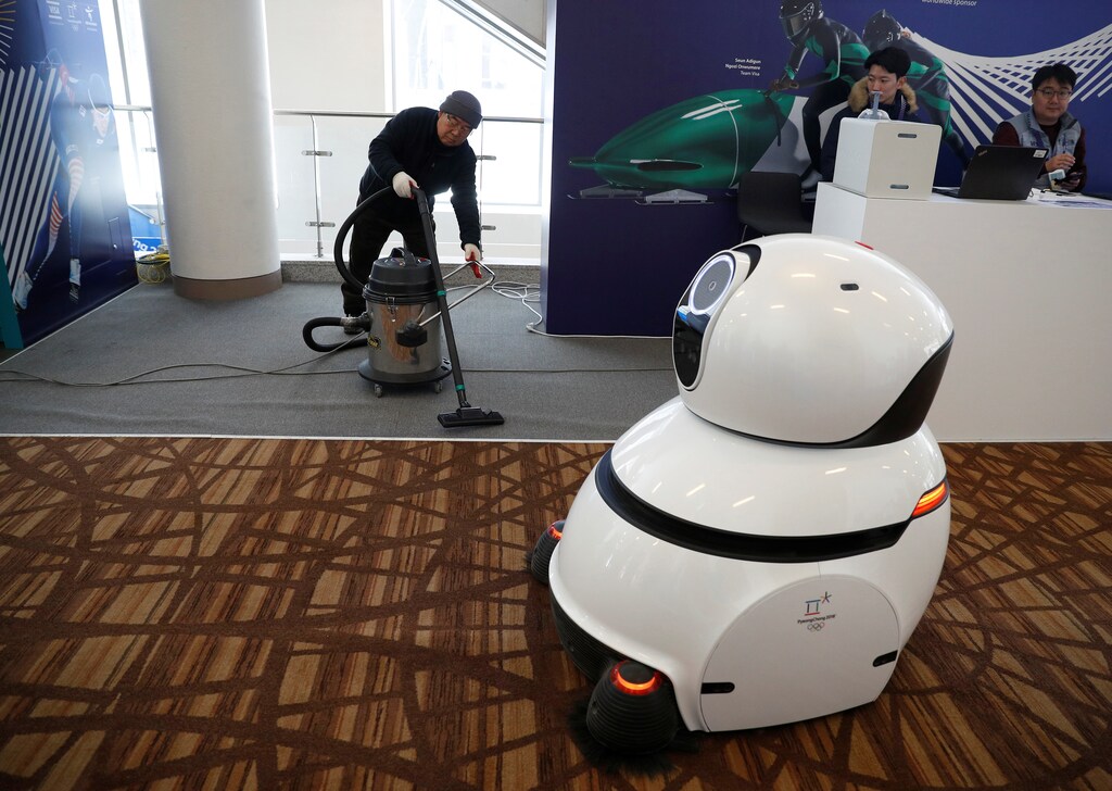 Pyeongchang 2018 Winter Olympics - Alpensia Main Press Centre, South Korea - February 13, 2018. A robot carpet cleaner passes a worker using a traditional vacuum cleaner in the Main Press Centre. REUTERS/Phil Noble - RC11EFC938C0