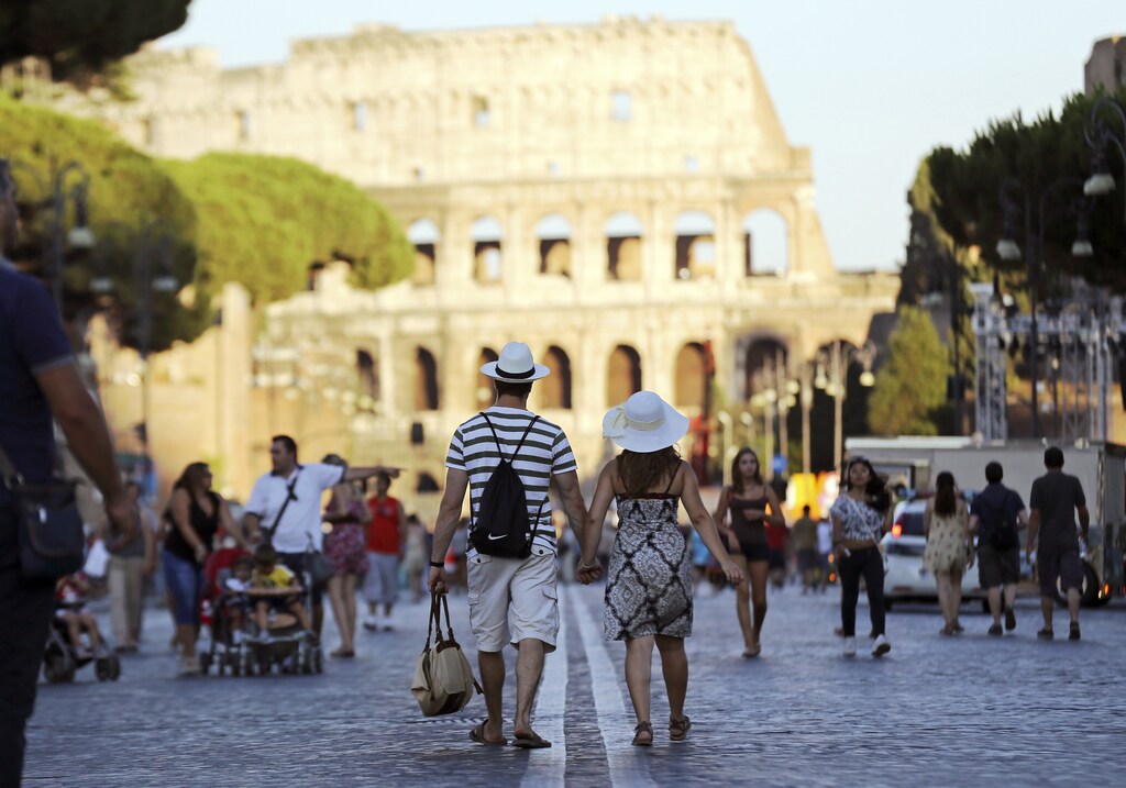 People walk at the Fori Imperiali street with Rome's famous colosseum in the background.