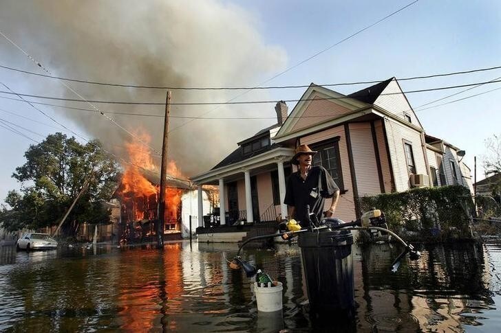 A man stands in flood waters as fire burns down a home in the seventh ward of New Orleans in the aftermath of Hurricane Katrina September 6, 2005. The toxic brew of chemicals and human waste in the New Orleans floodwaters will have to be pumped into the Mississippi River or Lake Pontchartrain, raising the specter of an environmental disaster on the heels of Hurricane Katrina, experts say. Pictures of the Year 2005 REUTERS/Shannon Stapleton SS/CN