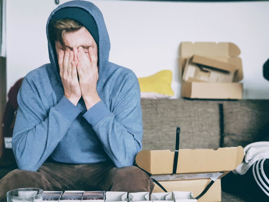 A person in a hooded top sitting on the couch, visibly destressed.