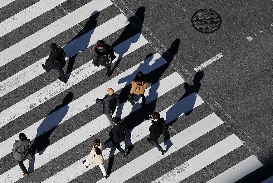 Pedestrians cast shadows on the crosswalk near the headquarters of the Bank of Japan in Tokyo December 19, 2014. The Bank of Japan maintained its massive monetary stimulus on Friday and offered a brighter view of the economy, clinging to hope that joint efforts with Prime Minister Shinzo Abe to revitalise the economy will prod companies into boosting wages and investment.