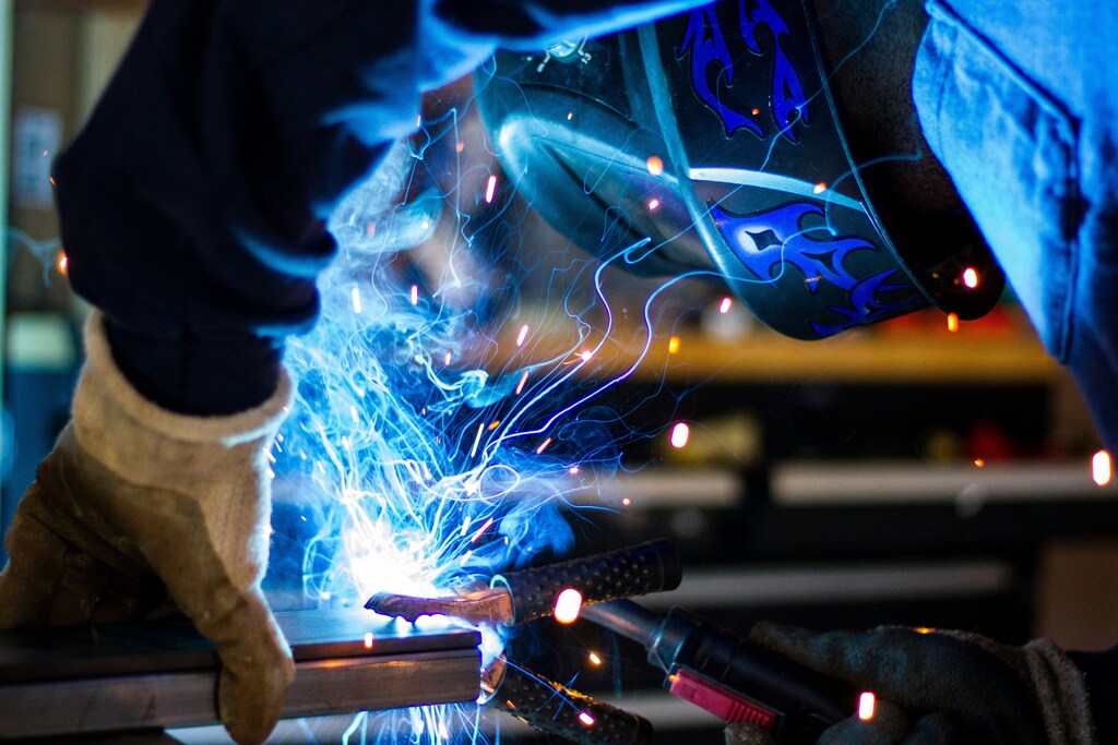 Man holding tray steel frame with blue sparks: Industrial electrification can only scale if partnerships are forged involving banks and energy companies.