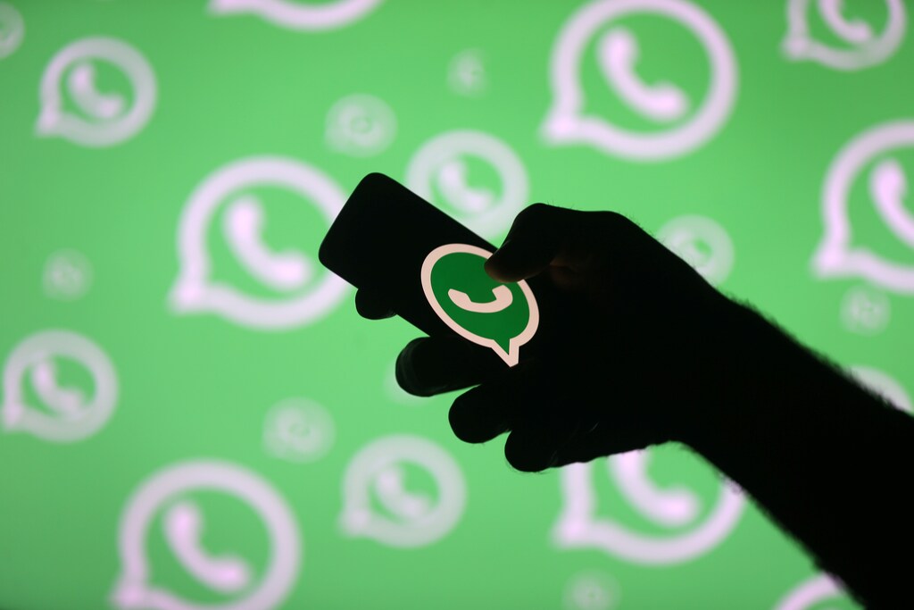 A man poses with a smartphone in front of displayed Whatsapp logo.