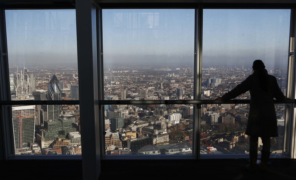 A woman looks out at the financial district from a window in The View gallery at the Shard, western Europe's tallest building, in London January 9, 2013. The View, the public viewing deck accessible by high speed elevators on the 309 metre (1,013 feet) Shard building, opens on February 1. Picture taken January 9, 2013. REUTERS/Luke Macgregor (BRITAIN - Tags: TRAVEL CITYSCAPE) - LM1E91A0RM901