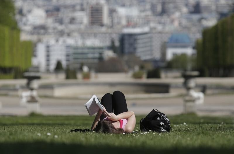 A woman reads a book as she enjoys a sunny and warm spring day at the Parc de Saint-Cloud, outside Paris, April 13, 2015. REUTERS/Christian Hartmann - RTR4X5QD
