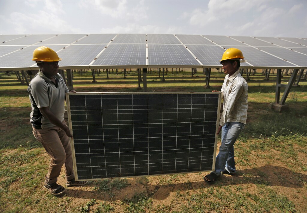 Workers carry a damaged photovoltaic panel inside a solar power plant in Gujarat, India, July 2015.