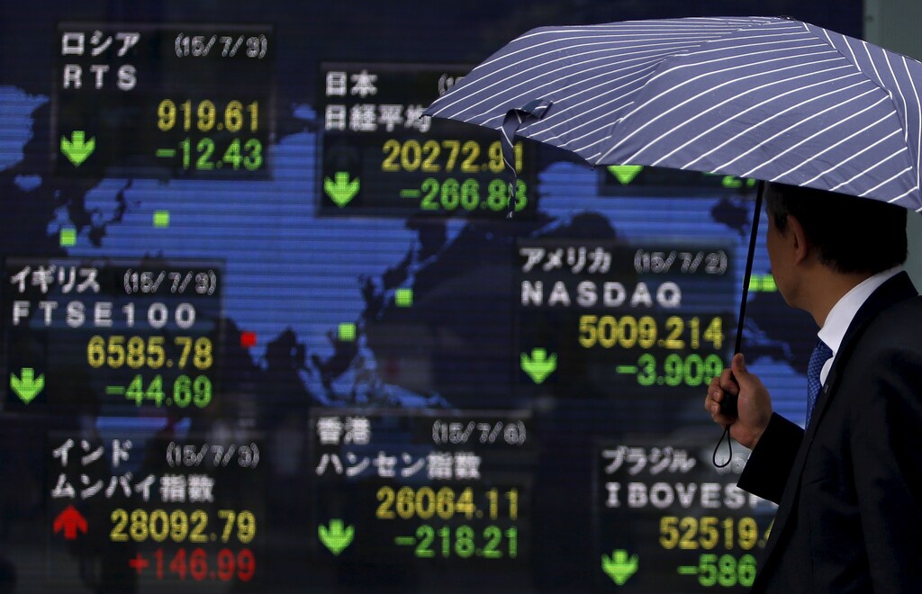 A pedestrian holding an umbrella looks at an electronic board the stock market indices of various countries outside a brokerage in Tokyo, Japan, July 6, 2015. The euro and stock prices fell sharply in Asia on Monday after the Greeks had overwhelmingly rejected austerity measures demanded in return for bailout money, putting in doubt its continued place in the single currency. U.S. equity futures dropped around 1.4 percent while Japan's Nikkei shares fell 1.4 percent and MSCI's broadest index of Asia-Pacific shares outside Japan dropped 0.5 percent. REUTERS/Yuya Shino - GF10000149956