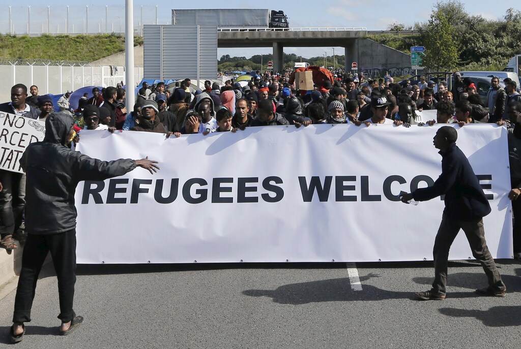 Migrants and refugees hold a banner which reads, "Refugees Welcome" with members of refugee aid organisations in the encampment known as the "New Jungle" during a demonstration of solidarity in Calais, France, September 19, 2015. French authorities say more than 3,000 people fleeing war and poverty in the Middle East, Africa and Asia now live in the jungle, with most trying to find a way to cross to England. REUTERS/Regis Duvignau - RTS1VPV
