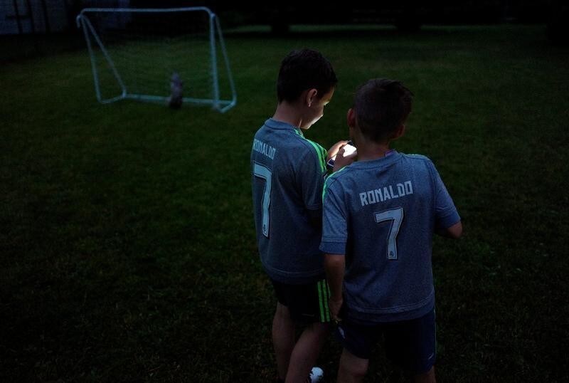 Boys, wearing Real Madrid football kit with Cristiano Ronaldo's name, play a soccer game on their mobile phones as their parents watch a telecast of the Champions League final between Juventus and Real Madrid at a local Spanish restaurant in the city of Hanau, Germany, June 3, 2017.