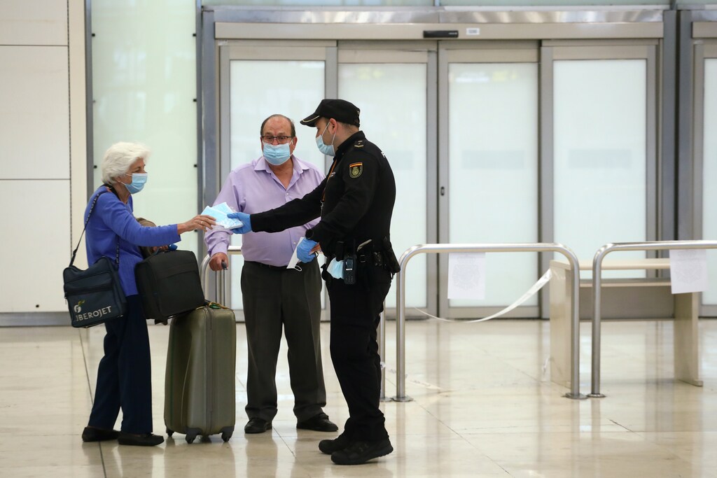 Los pasajeros recogen máscaras faciales de protección de un oficial de la Policía Nacional al llegar al aeropuerto Adolfo Suárez Barajas, después de que el gobierno español anunciara que a partir del 15 de mayo todas las personas que entren en España tendrán que estar en cuarentena durante dos semanas, en medio del brote de la enfermedad coronavirus (COVID-19) en Madrid, España, el 12 de mayo de 2020. Traducción realizada con la versión gratuita del traductor www.DeepL.com/Translator