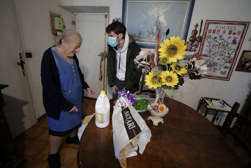 Bastien Gambaudo, joven miembro de la asociación de vecinos El Comité de la Vieja Niza, lleva bolsas de supermercado a una anciana mientras ofrece ayuda para la compra a las personas mayores y aisladas que viven en la vieja ciudad de Niza, durante un encierro impuesto para reducir el ritmo de la enfermedad coronavirus (COVID-19) en Francia, el 26 de marzo de 2020.