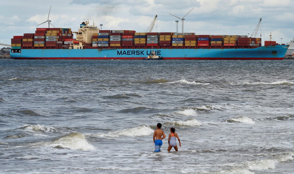 Children play in the sea at New Brighton as the Maersk Line container ship Maersk Sentosa is helped by tugs as it navigates the River Mersey in Liverpool, Britain, July 31, 2018. REUTERS/Phil Noble