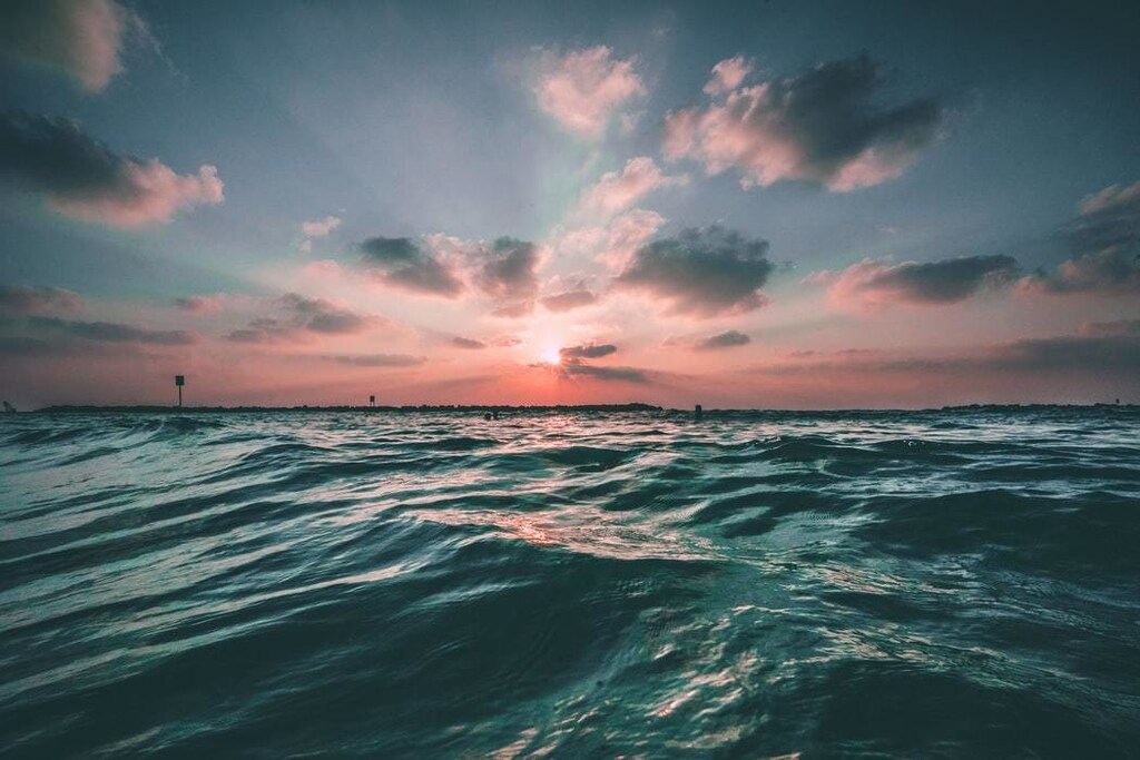 A photo of an ocean with the sun setting in the background.