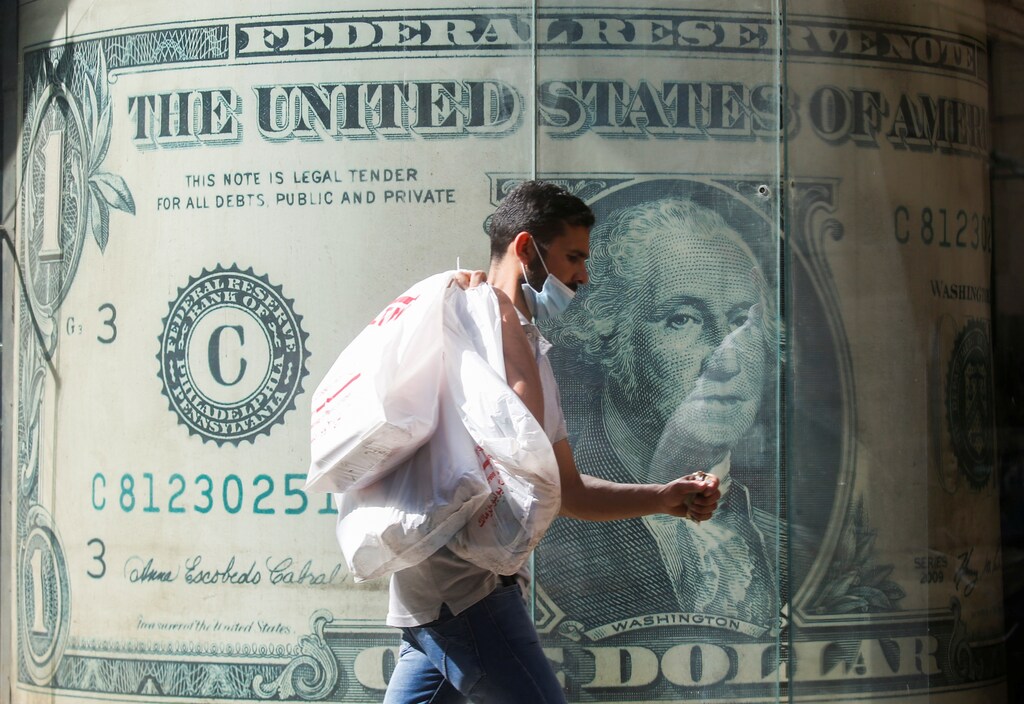 A man wearing a protective face mask walks in front of a currency exchange bureau advertisement showing an image of the U.S. dollar amid the coronavirus disease (COVID-19) pandemic in Cairo, Egypt May 5, 2021. REUTERS/Amr Abdallah Dalsh - RC2O9N9NA76Z