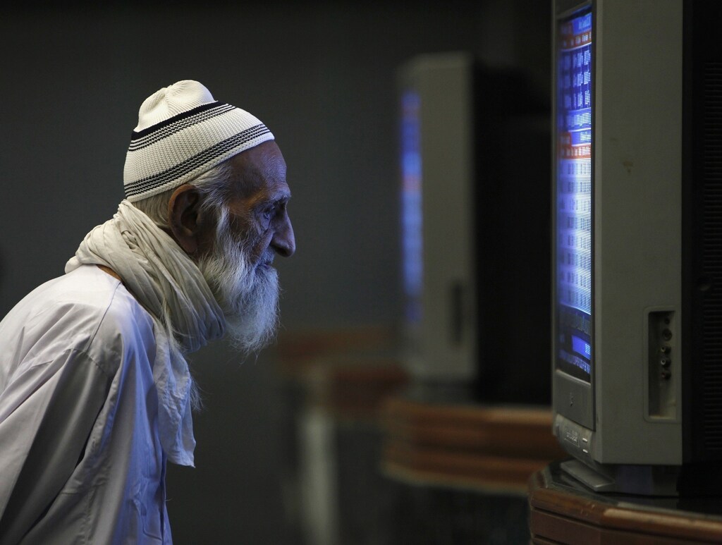 An elderly man monitors share prices on a television screen during a trading session inside the Karachi Stock Exchange December 20, 2010. REUTERS/Akhtar Soomro (PAKISTAN - Tags: BUSINESS IMAGES OF THE DAY) - RTXVWDZ