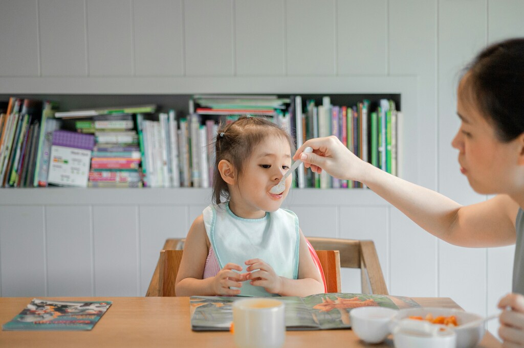 A young child sitting in a high chair being fed with a spoon, demonstrating healthy childhood nutrition.