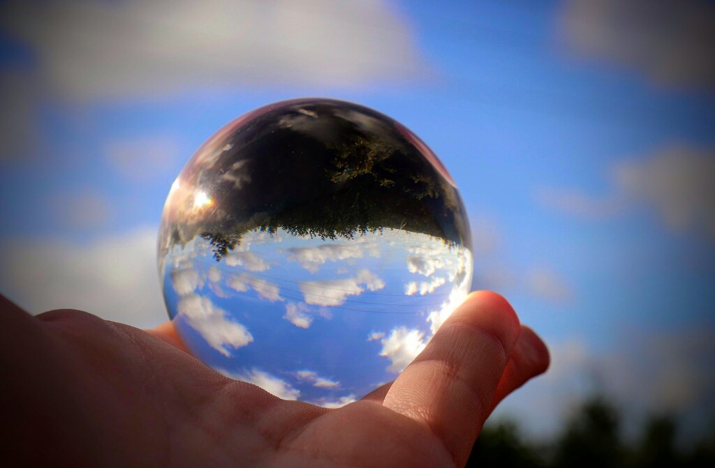 Hand holding glass sphere reflecting sky and earth
