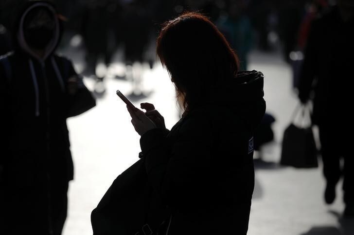A woman checks her phone as passengers arrive at the Beijing Railway Station as the annual Spring Festival travel rush begins ahead of the Chinese Lunar New Year, in central Beijing, China February 1, 2018. REUTERS/Damir Sagolj