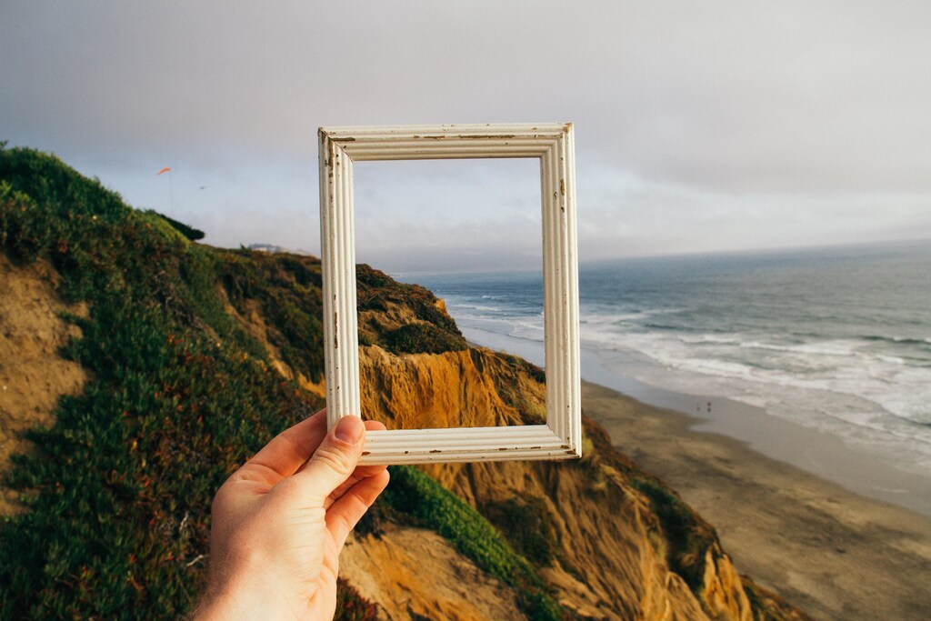 Cliffs, beach and sea scene, hand holding white frame; reframing the scene.