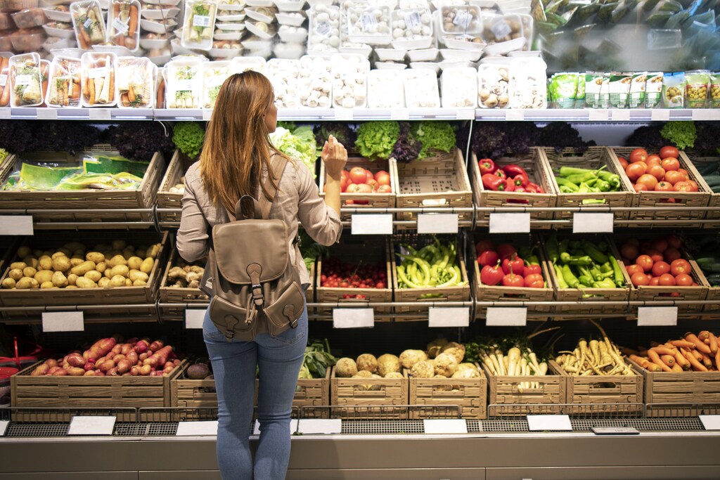 Woman standing in front of vegetable shelves choosing what to buy.