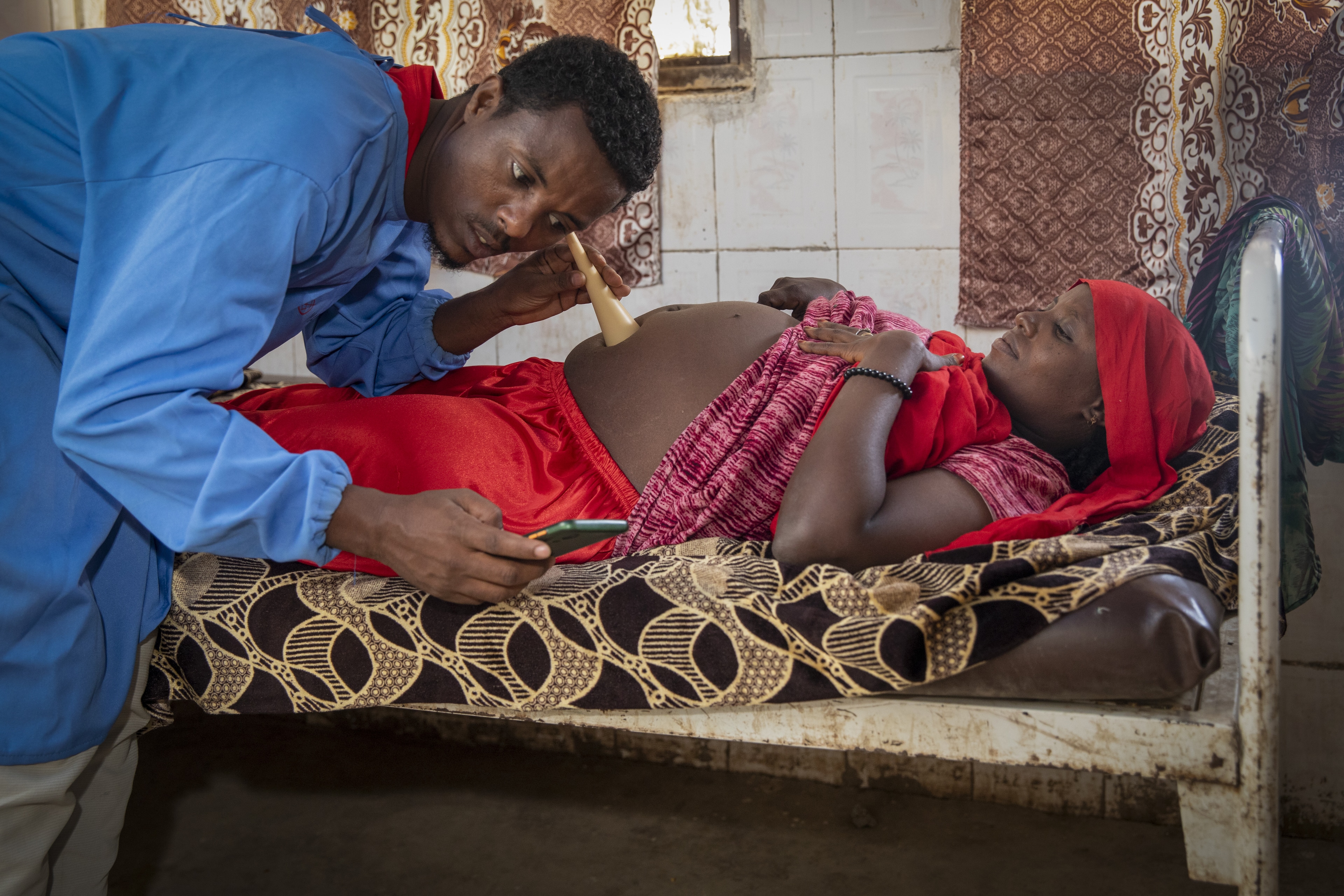 Midwife examines patient, pregnant women, smart phone; maternal health.