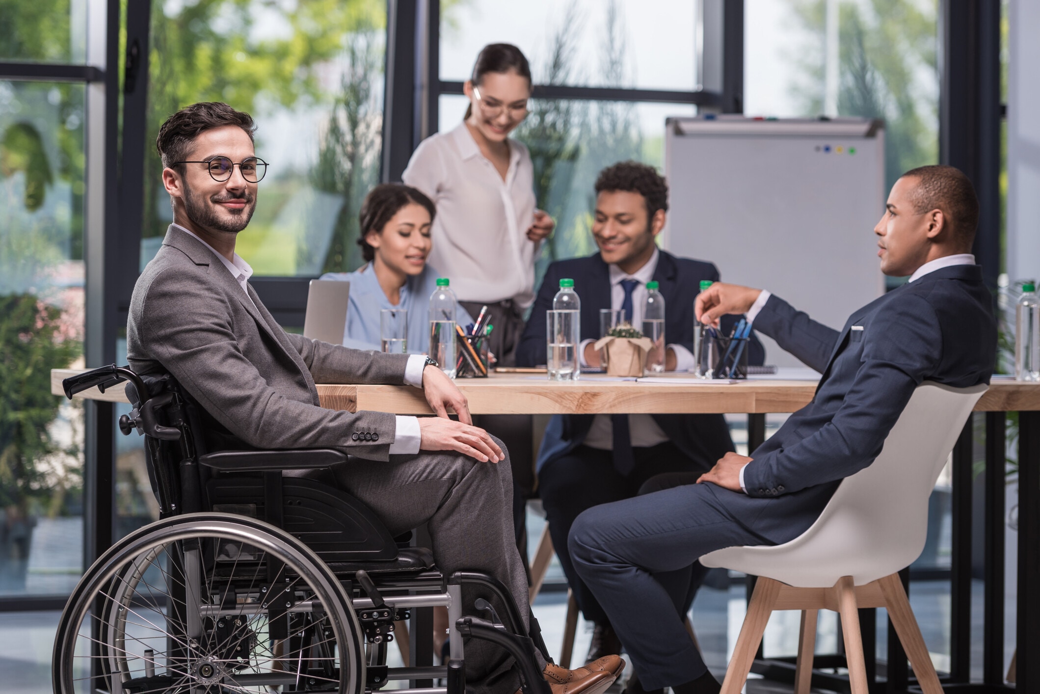 Selective focus of smiling disabled businessman looking at camera while colleagues discussing work: Managers need the skills to effectively deal with employee mental health and well-being.