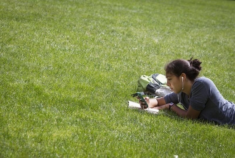A woman lies in the grass reading a book and listening to music at Columbia University in New York, April 14, 2014.