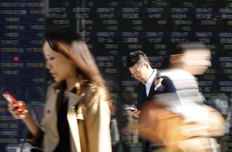 Pedestrians using their mobile phone walk past an electronic board displaying various stock prices outside a brokerage in Tokyo October 17, 2014. Asian stocks clawed back some of this week's losses on Friday after a solid set of U.S. data calmed turbulence in global financial markets, though underlying worries about slowing world economic growth kept investors on edge. REUTERS/Yuya Shino (JAPAN - Tags: BUSINESS) FOR BEST QUALITY IMAGE ALSO SEE: GF10000196185 - GM1EAAH117G01