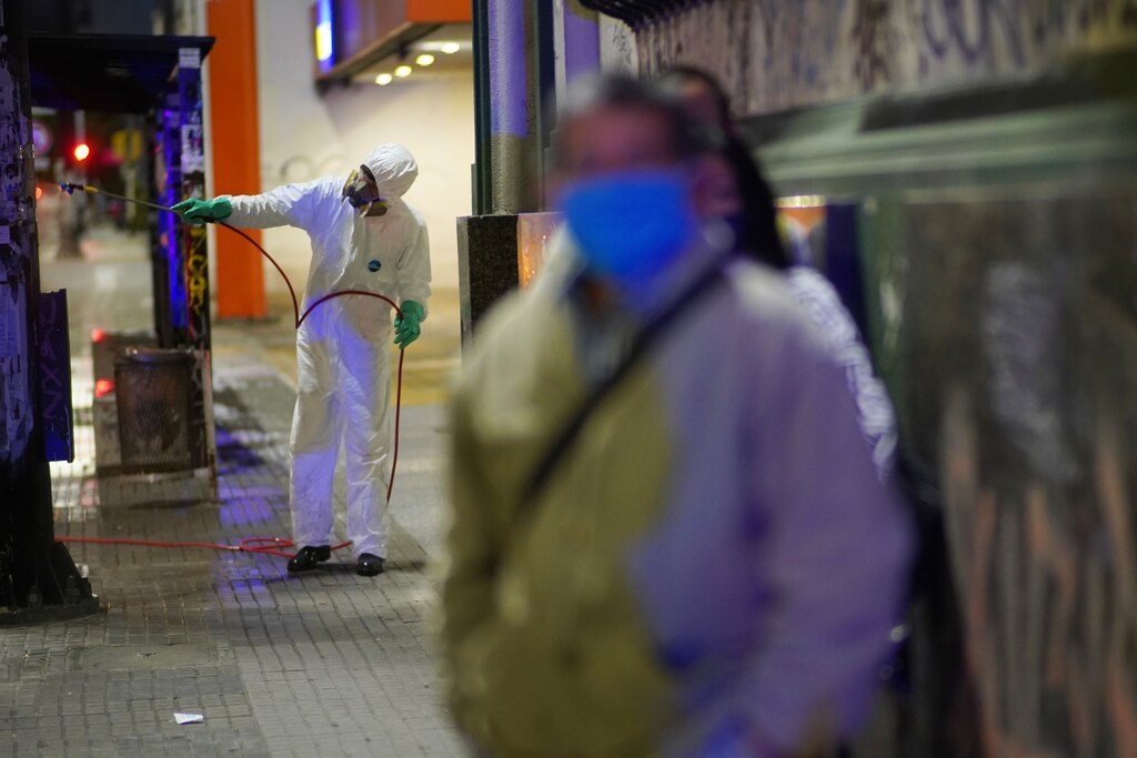 A municipal workers wearing personal protective equipment (PPE) disinfects an area around a bus stop as people wait, amid concerns about coronavirus disease (COVID-19) in, Montevideo, Uruguay April 19, 2020. REUTERS/Mariana Greif - RC238G9IGVZ9