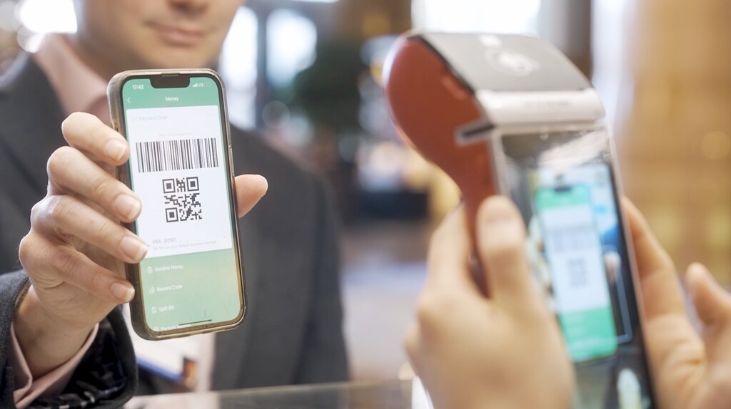 A man in a suit pays using a QR code on the mobile phone he is holding up to a terminal: Interoperability could be the next step towards seamless cross-border payments