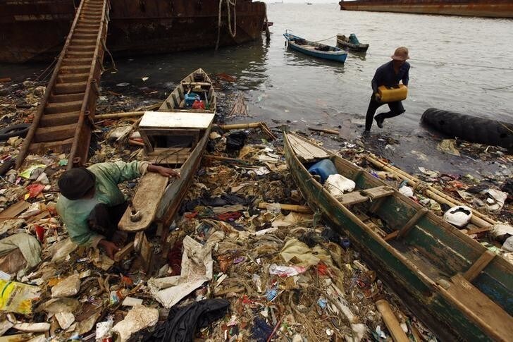 A fisherman (L) mends his boat as a fellow fisherman carries a box of fish at a polluted beach in Cilincing, North Jakarta June 5, 2013. The fisherman said that it has been difficult to catch fish in the last five years due to the pollution on the beach by plastic and garbage. World Environment Day is celebrated annually on June 5. REUTERS/Beawiharta (INDONESIA - Tags: ENVIRONMENT BUSINESS EMPLOYMENT SOCIETY)